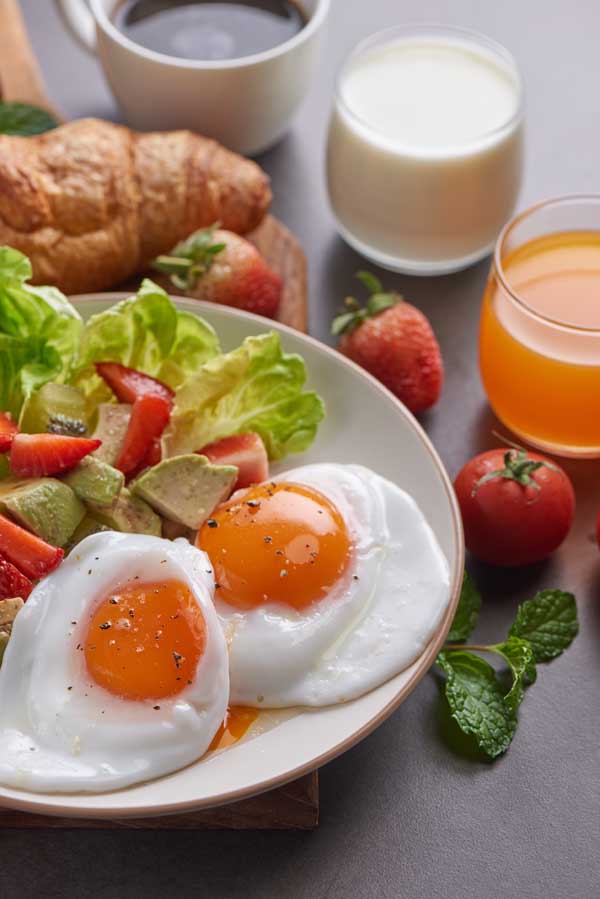 Delicious breakfast with fresh croissants and coffee served, Milk, orange juice. strawberry, Butterhead , kiwi, fried egg and avocado salad on a white dish on a cutting board. Healthy vegetarian food